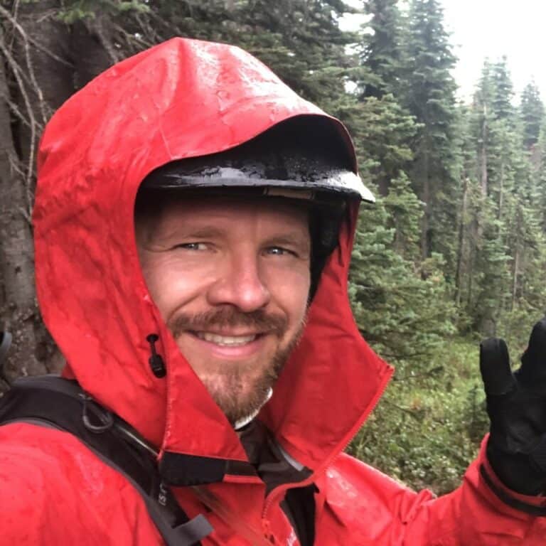 Bearded man smiling and waving wearing a red hooded raincoat