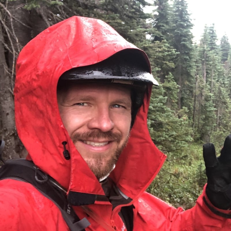 Bearded man smiling and waving wearing a red hooded raincoat