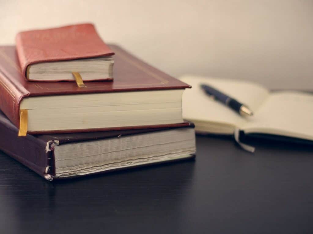 Three stacked leatherbound books in the foreground with a pen on top of an open book in the background